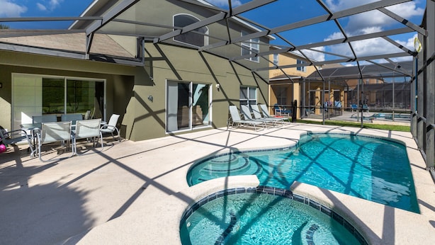 A pool area with a glass enclosure, lounge chairs, and a table. - Mickeys Encore by VillaDirect (Kissimmee)
