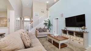 A spacious living room with a large sofa, a coffee table, and a TV on a stand. - Mickeys Encore by VillaDirect (Kissimmee)