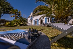 A poolside area with lounge chairs, a pair of sunglasses, and a house with blue shutters in the background. - Ti Nalu, a large family home near the beaches (Plouharnel)