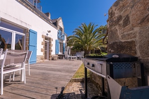 Um deck de madeira com área de estar ao ar livre, churrasqueira e uma parede de pedra.