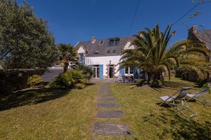 Uma casa com fachada de pedra, um jardim frontal pavimentado e uma palmeira.