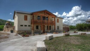 Une maison à deux étages avec une façade en pierre, un balcon en bois et une allée menant à l’entrée.