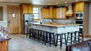 Une cuisine spacieuse avec des meubles en bois, un îlot central doté de tabourets et un plafond haut avec des poutres apparentes.