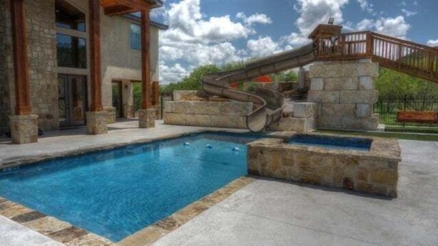 Une piscine avec un toboggan, une architecture en pierre et une terrasse en bois.