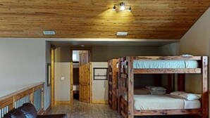 Une cabane avec une chambre à coucher située en mezzanine, un plafond en bois, un ventilateur de plafond, un banc en bois et un canapé en cuir.