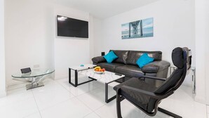Ett modernt vardagsrum med en soffa i läder, ett soffbord i glas, en svart stol och en tv med platt skärm.