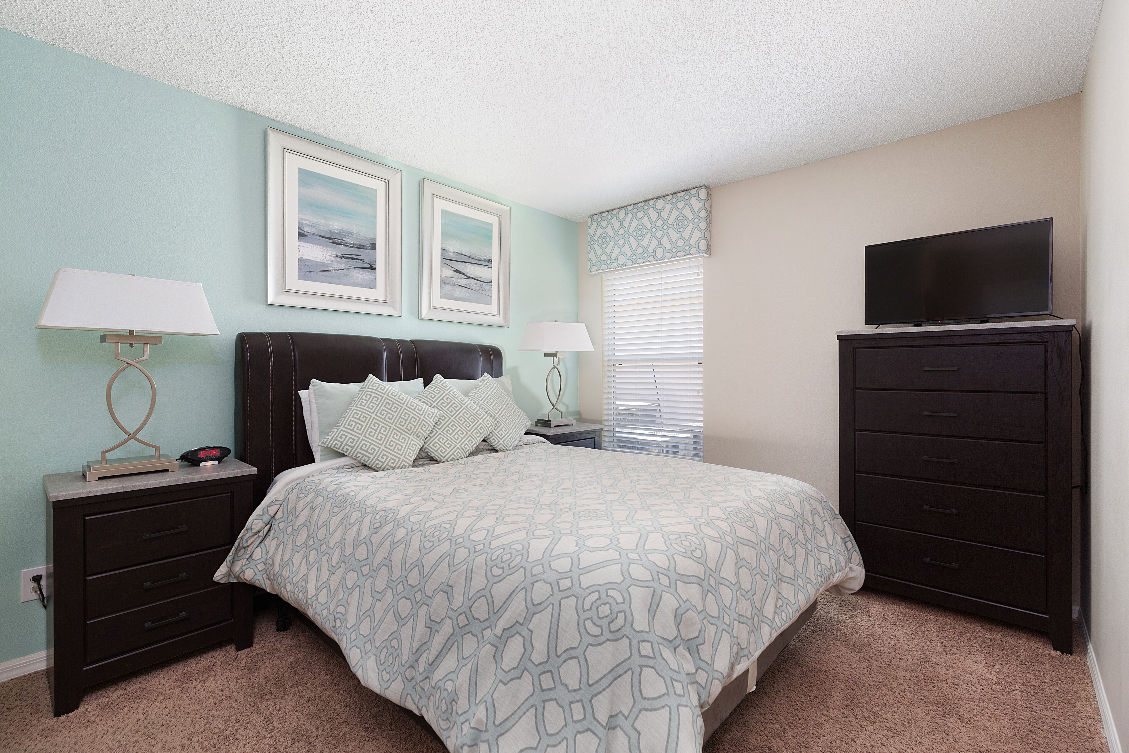 A bedroom with a bed, two bedside tables with lamps, a dresser, and a television on top.