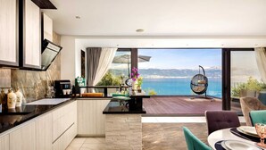 A modern kitchen with a view of the sea, a dining area with a table set for two, and a hanging chair. - Villa Arbanessa with Heated Pool (Arbanija)