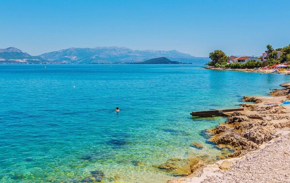 Eine Küstenansicht mit klarem türkisblauem Wasser, felsiger Küstenlinie und fernen Bergen.