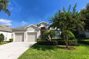 A two-story residential house with a front driveway, two garage doors, and a well-maintained lawn with a small tree.