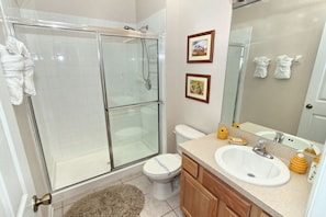 A bathroom with a glass-enclosed shower, a toilet, a sink with a mirror, and framed pictures on the wall.