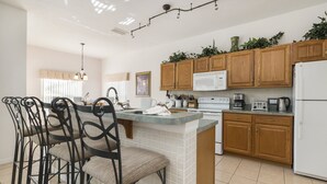 A modern kitchen with wooden cabinets, a central island, and a dining area with metal chairs.
