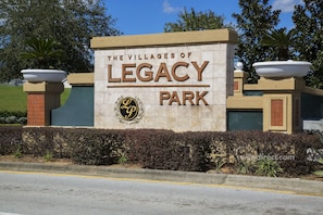 A sign for The Villages of Legacy Park with a logo and a landscaped area with plants and a palm tree.