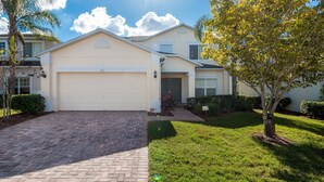 A two-story house with a white garage door, a brick driveway, and a well-maintained lawn with a tree.