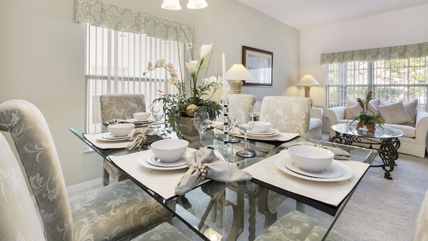 A dining area with a glass table, chairs, and a chandelier. There are dining tables with white tablecloths and plates.