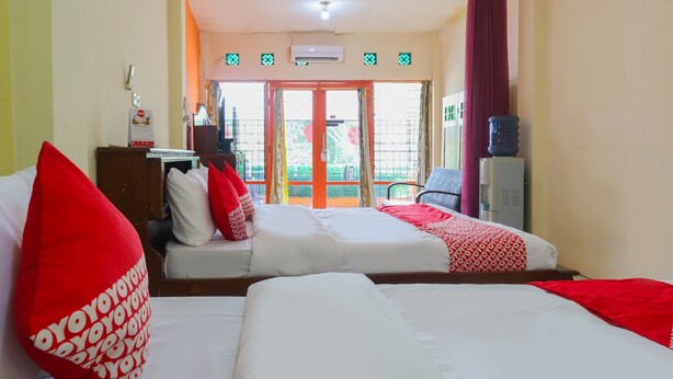 Ein Hotelzimmer mit zwei Betten, Bettwäsche in Rot und Weiß, einem Wasserspender und Blick durch eine Glastür.
