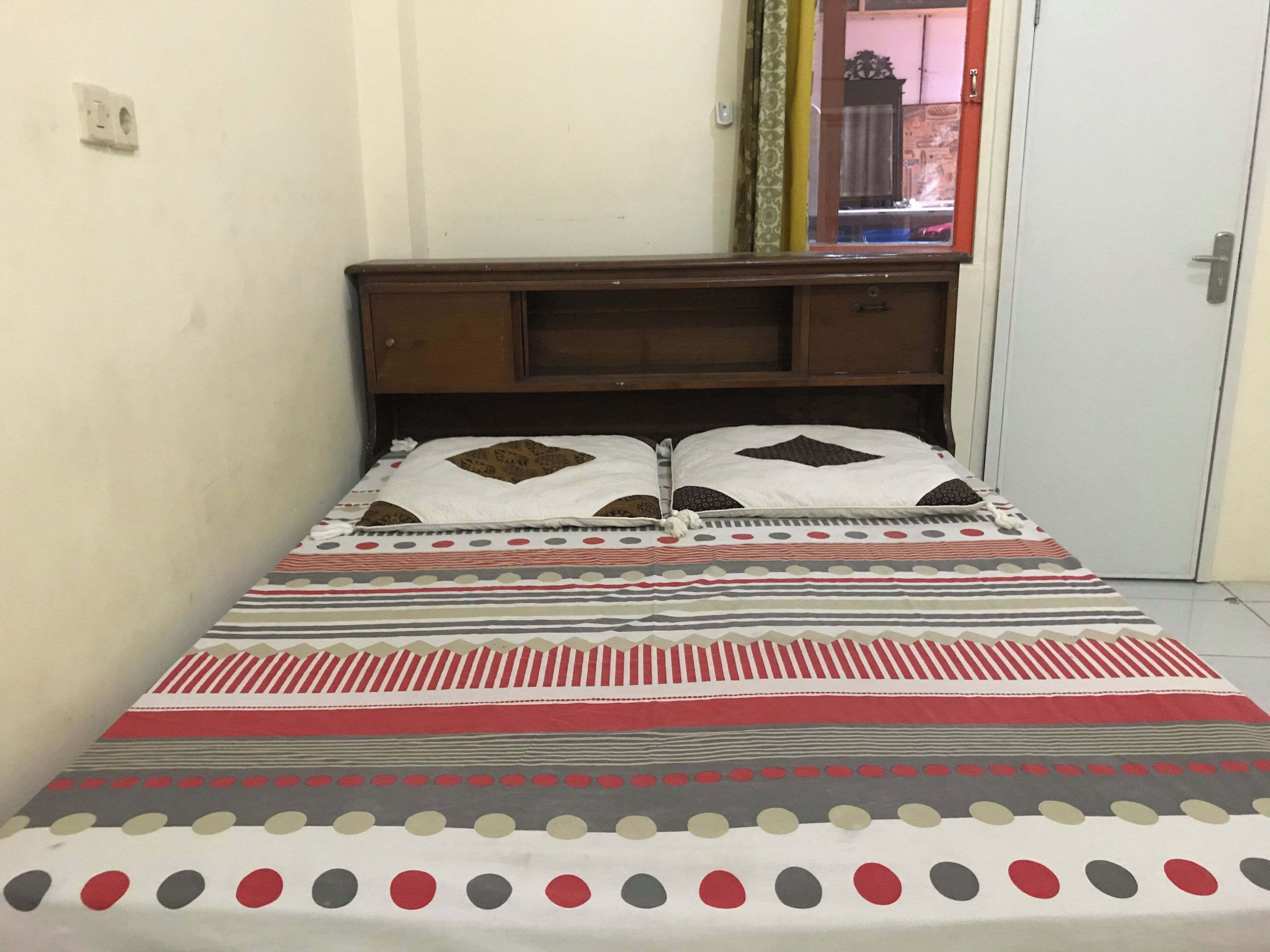 Een bed met een beddegoed met patroon, een houten hoofdbord en een spiegel aan de muur.