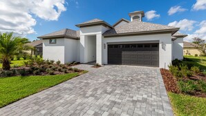 A modern two-story house with a paved driveway, a garage, and landscaped gardens. - Paradise at Providence by VillaDirect (Davenport)