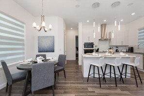 A modern kitchen with a central island, pendant lighting, and a dining area with grey chairs.
