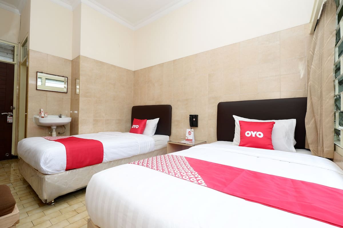 A hotel room with two beds, a bedside table, a mirror, a sink, and a window with curtains.