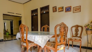 A dining area with a glass-top table, wooden chairs with floral upholstery, and a tiled floor. - Hotel O Maya (Beru)