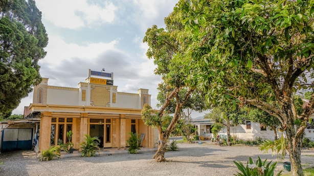 A building with a sign reading "LATE HOTEL SPOT ON." It features a courtyard with gravel, potted plants, and a large tree. - Hotel O Maya (Beru)