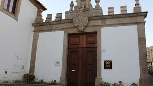 A building with a large wooden double door, a stone wall with a crest, and a sign that reads "SOLAR AREA". - Solar Do Areal (Braga)