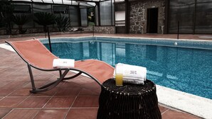 A pool area with a lounge chair and a small table with towels and a glass of juice. - Solar Do Areal (Braga)