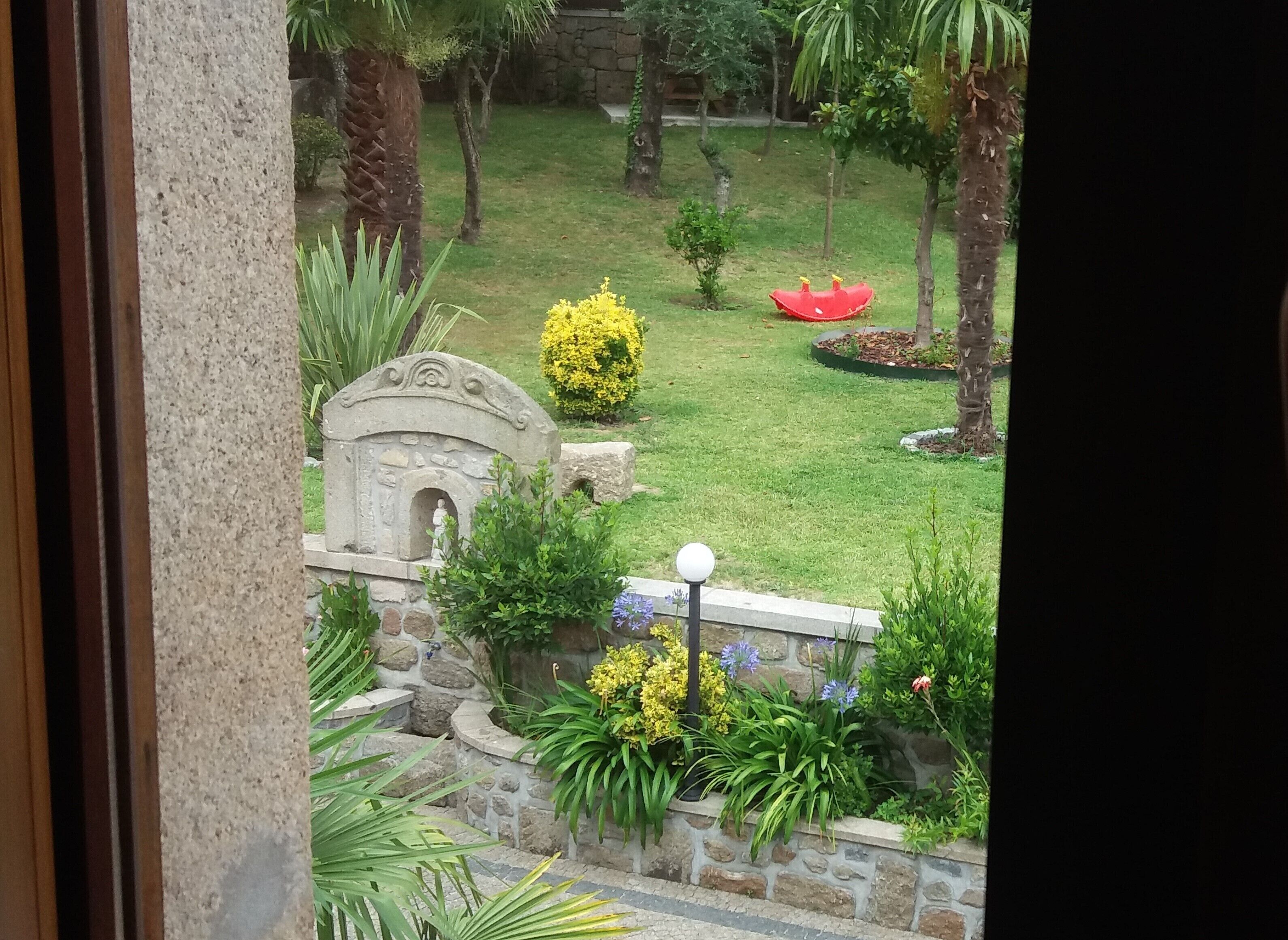 A stone pathway leading to a small garden with a statue, a red boat-shaped planter, and various shrubs.