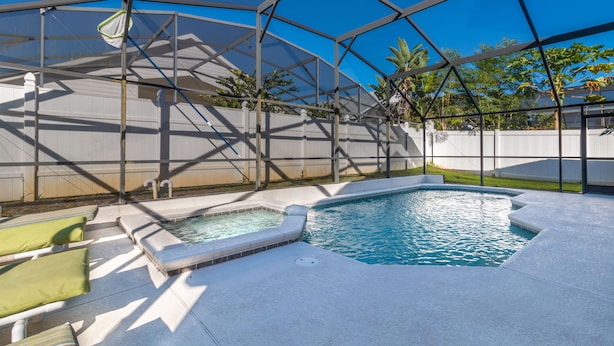 Una piscina con un jacuzzi, rodeada por un área techada con sillones de descanso.