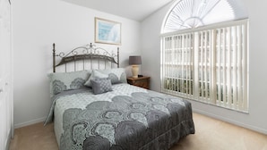 Un dormitorio con cama, mesita de noche, lámpara, ventana con persianas y ventilador de techo.