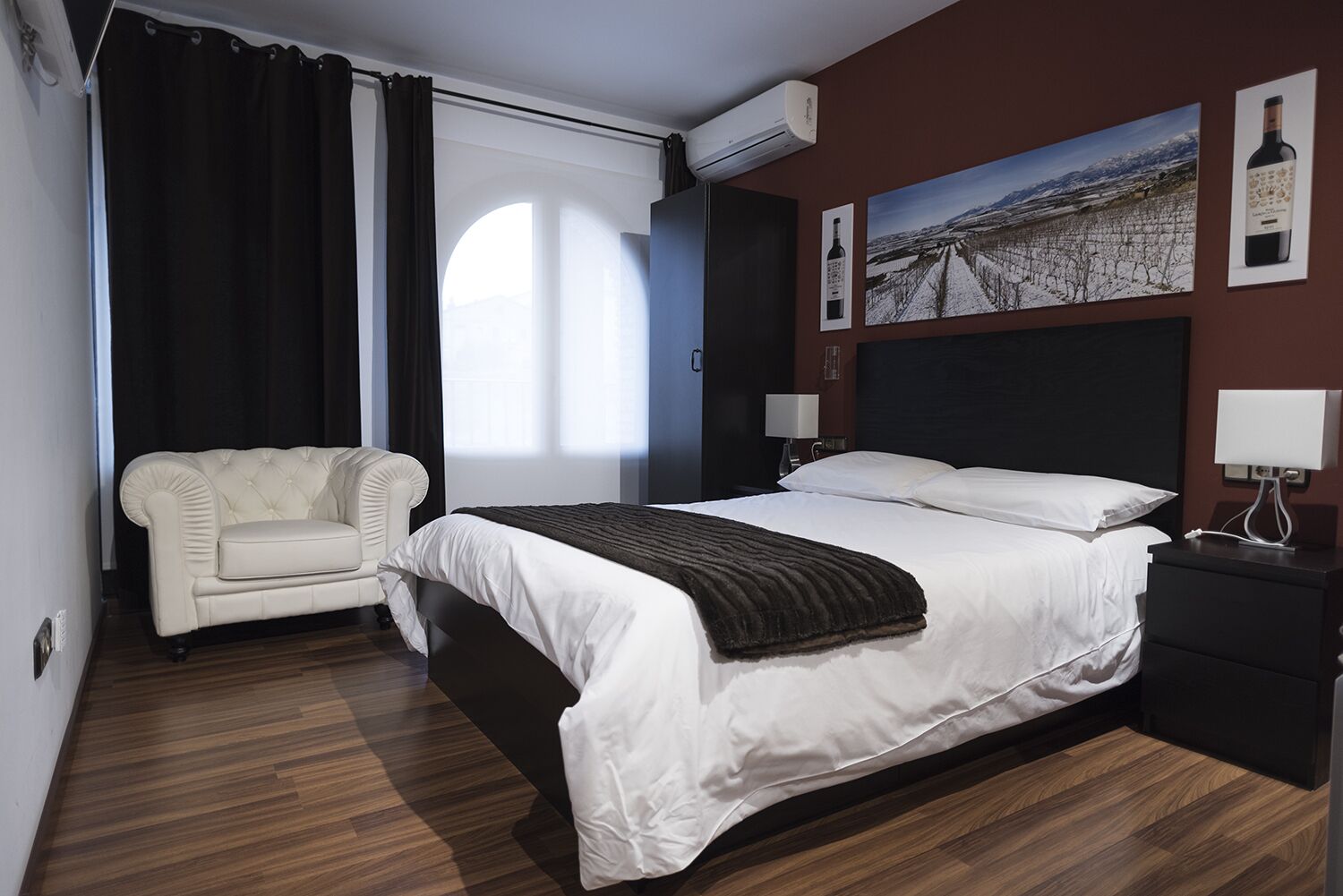 A hotel room with a large bed, a chair, a nightstand, and a wall-mounted air conditioner.