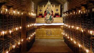 An ornate church interior with a central altar, rows of candles, and a statue of a religious figure.