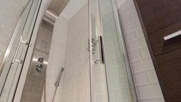 A glass-enclosed shower with a handheld showerhead and a wall-mounted control panel.