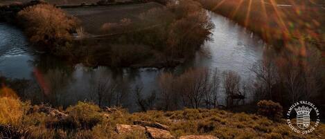 A river landscape with a sunset, hills in the background, and a logo in the bottom right corner.