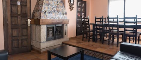 A cozy living room with a fireplace, a dining area with chairs, and a large window.