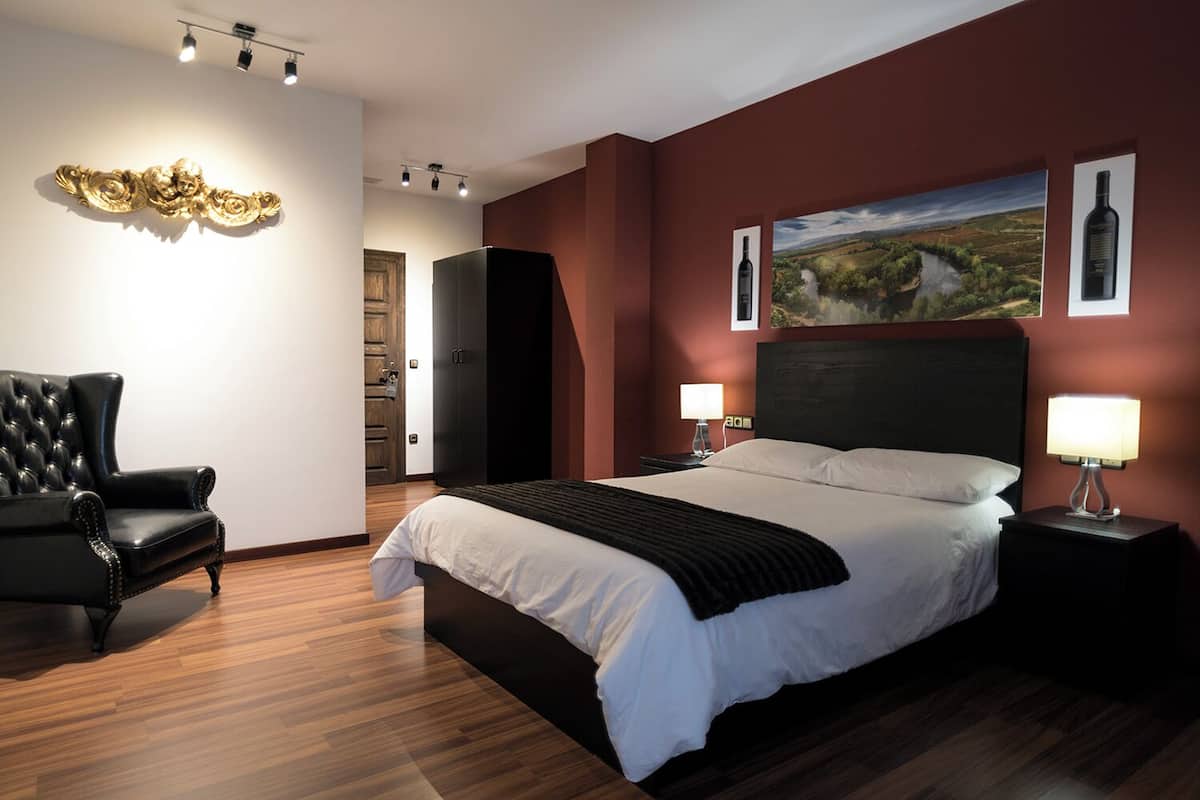 A modern bedroom with a large bed, a leather armchair, and artwork on the walls.