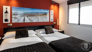 Een hotelkamer met een groot bed, twee nachtkastjes, een lamp en een groot schilderij in een lijst aan de muur.