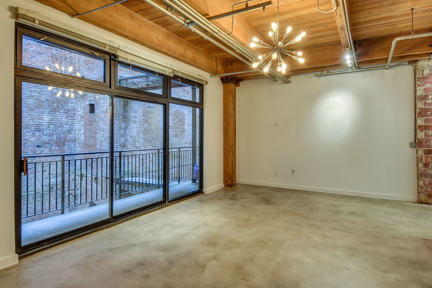 A spacious room with large windows, exposed wooden beams, and a concrete floor.