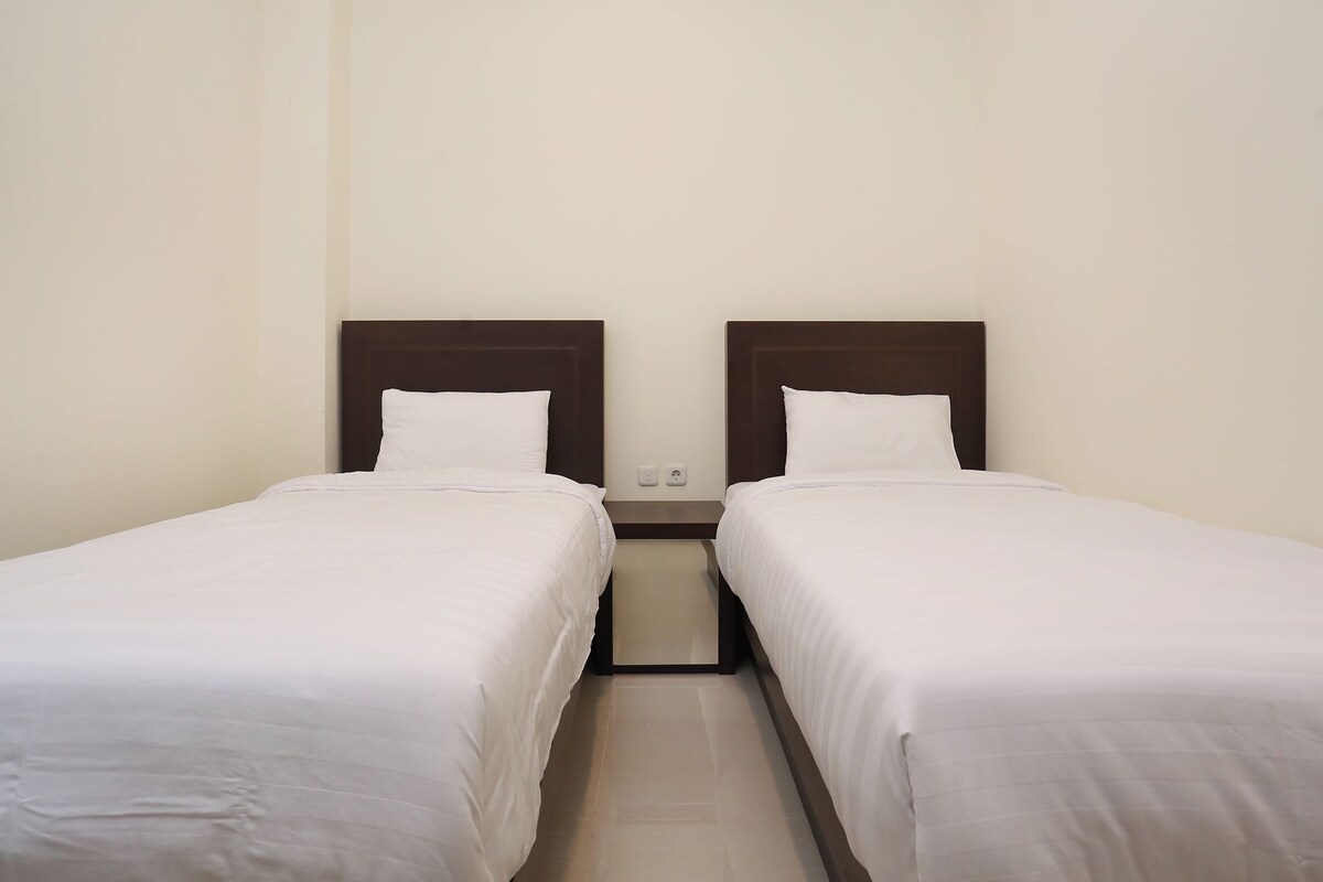 Habitación doble con dos camas individuales, una mesita de noche entre ellas y un enchufe en la pared.
