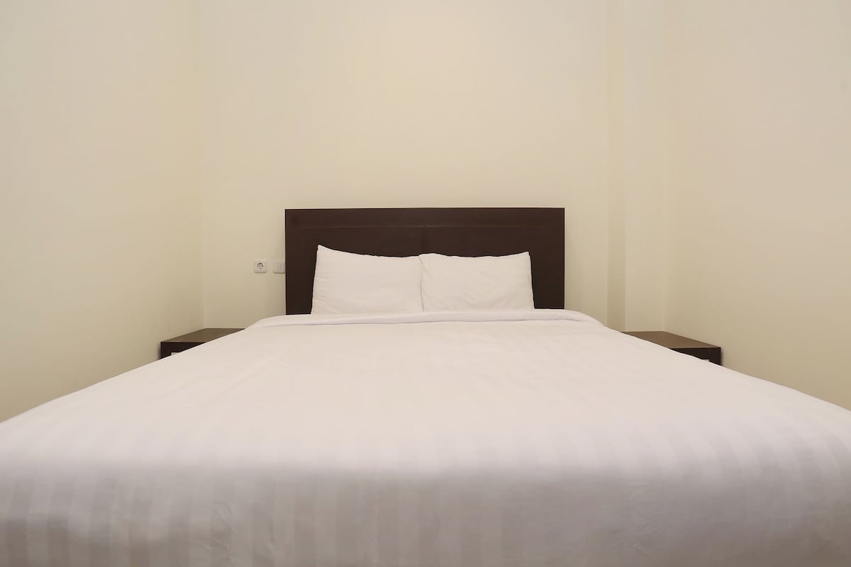 Una cama individual con cabecera de madera y ropa de cama blanca en una habitación sencilla.