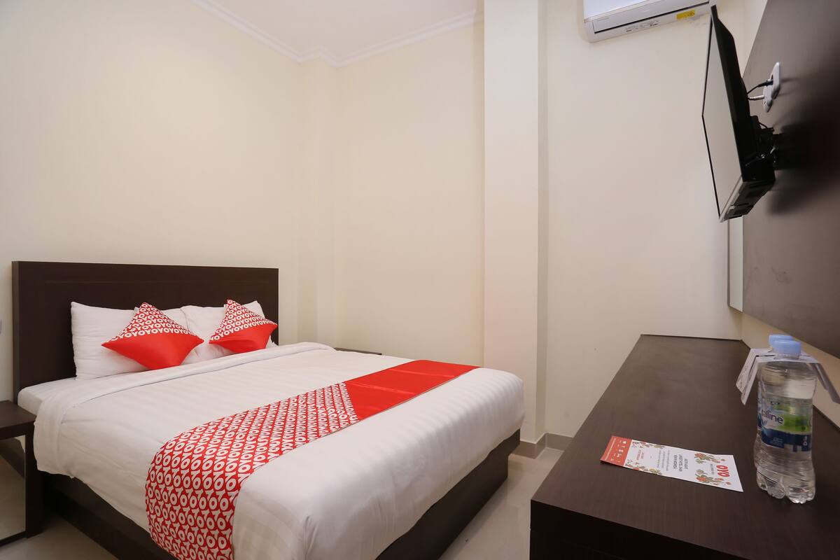 Habitación de hotel con cama, mesita de noche, mesa de madera, botella de agua y aire acondicionado de pared.