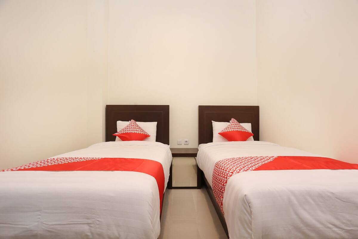 Habitación de hotel con dos camas individuales, cada una con cubrecama blanco y almohadas rojas.