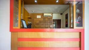 Mostrador de recepción con detalles de madera y toques rojos, un cartel arriba y piso de baldosas.