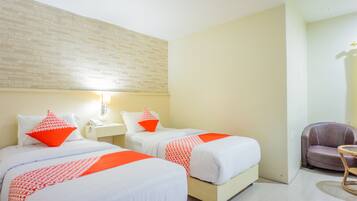 Quarto de hotel com duas camas, uma mesa pequena, uma cadeira e parede com padrão de tijolos.