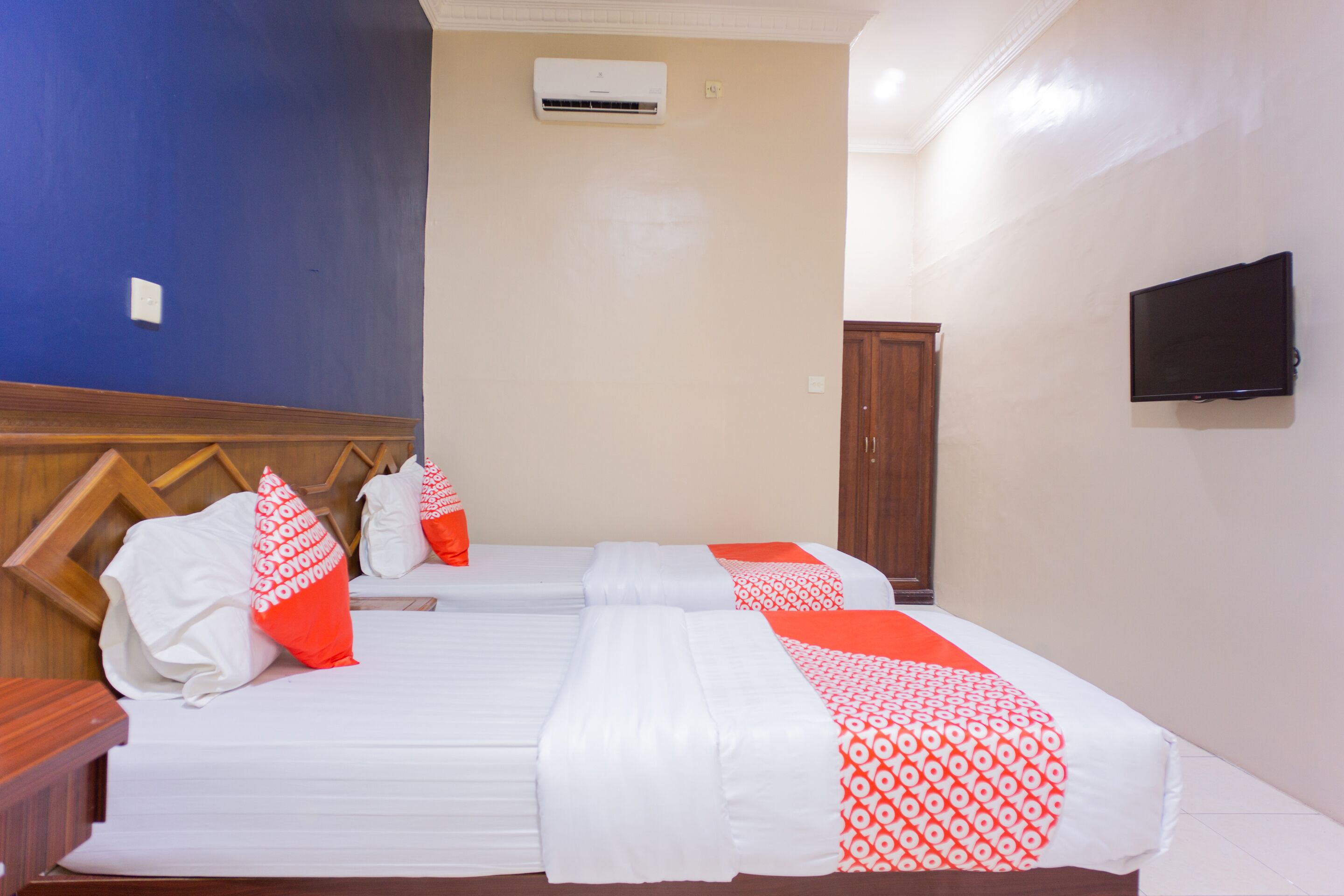 A hotel room with two beds, a TV, and an air conditioning unit.