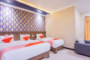A hotel room with two beds, a sofa, and a patterned wall. - Hotel O Wisma Kuta Karang (Lhokseumawe)