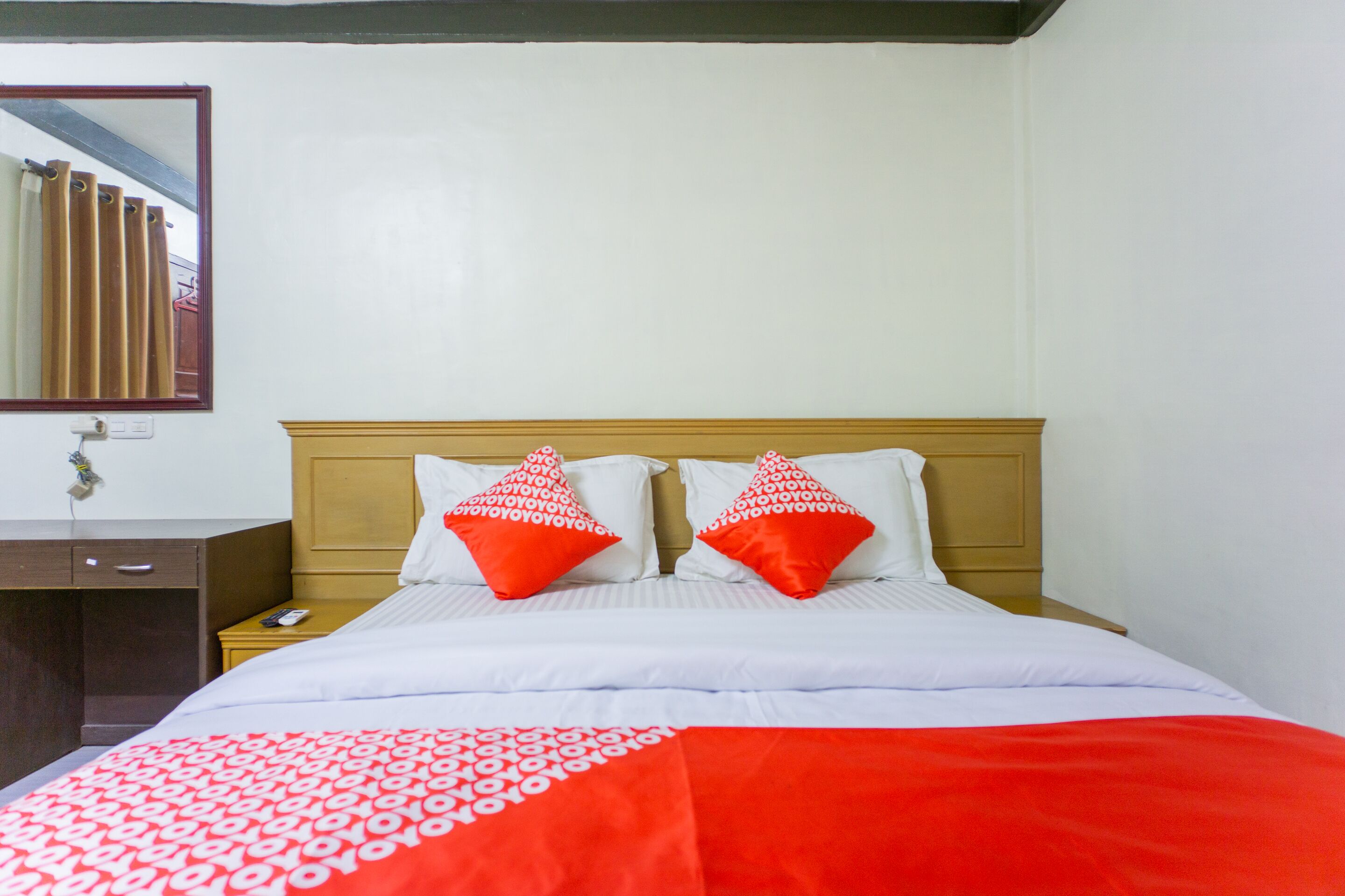 Une chambre d’hôtel avec une tête de lit en bois, du linge de lit blanc et deux oreillers rouges ornés d’un motif blanc.