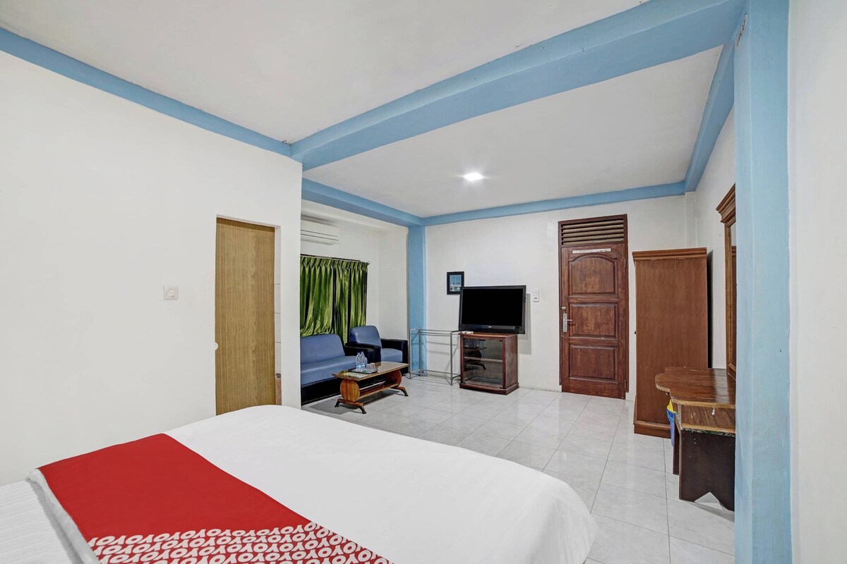Quarto de hotel com cama, televisão, sofá, escrivaninha e porta.