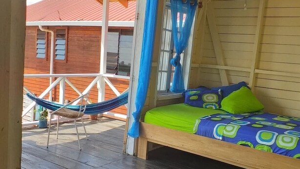 A wooden cabin with a bed, a hammock, and a view of a red-roofed building. - Life Is Good Casa (Bocas del Toro)